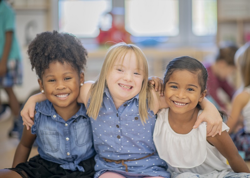 three girls sitting and smiling together looking at camera